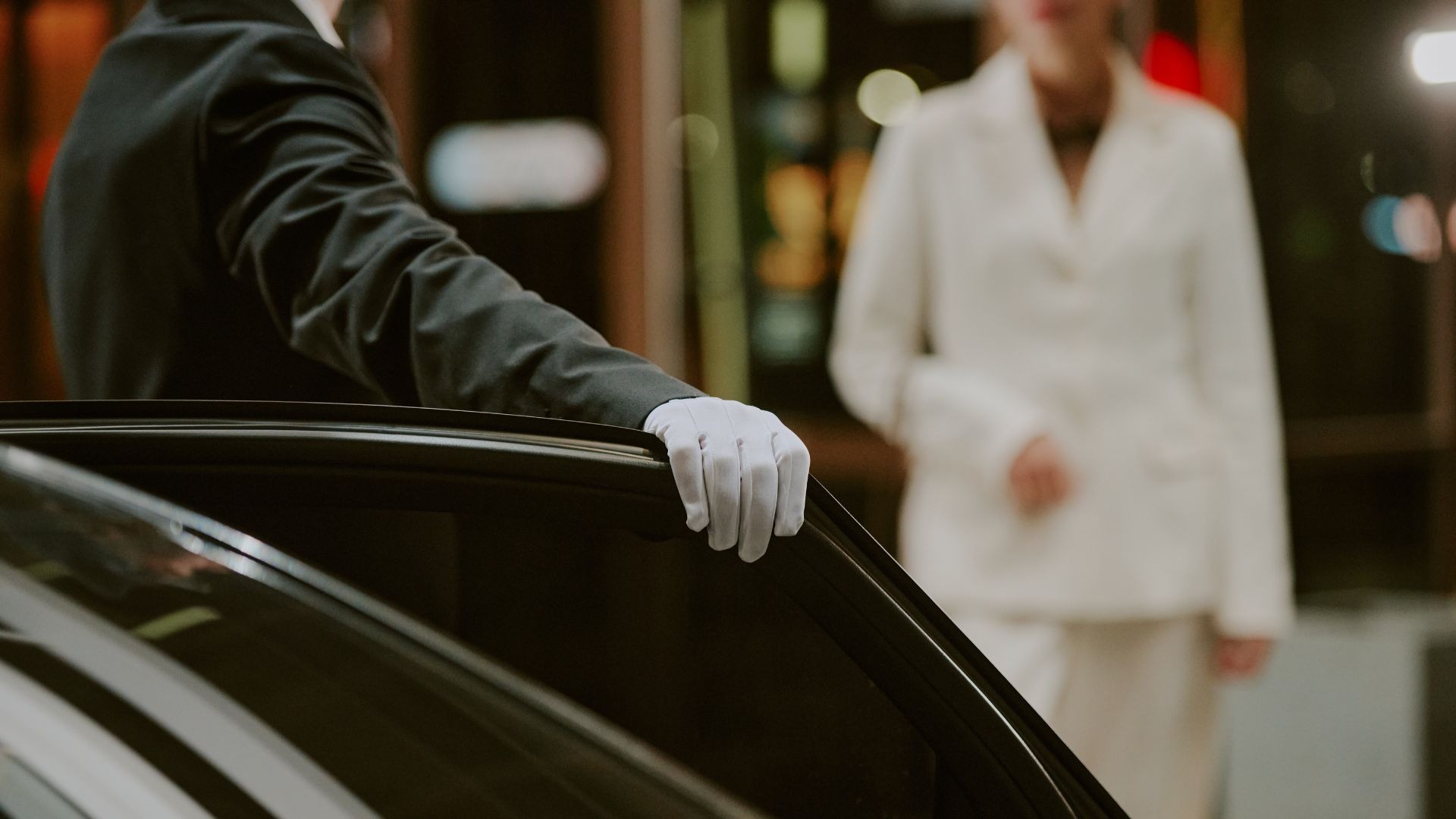 Private chauffeur holding door open for passenger outside grand hotel